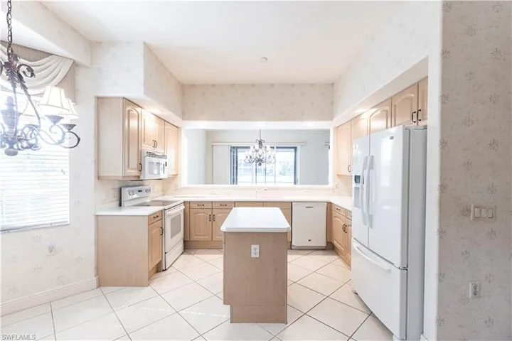 Kitchen featuring white appliances, light brown cabinets, a chandelier, a sink, and wallpapered walls