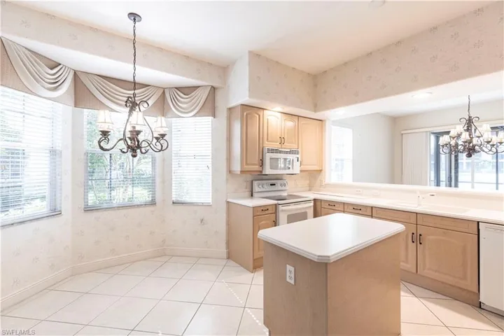 Kitchen with white appliances, a chandelier, a sink, light brown cabinetry, and wallpapered walls
