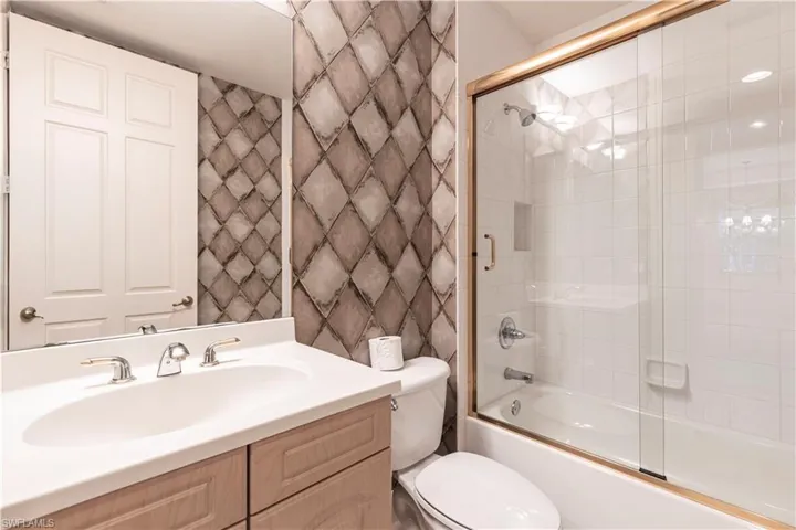 Bathroom with toilet, shower / bath combination with glass door, and vanity