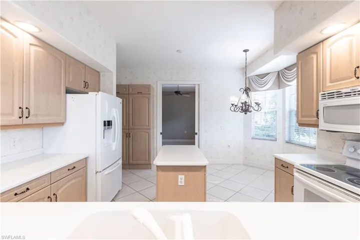 Kitchen featuring white appliances, wallpapered walls, light brown cabinetry, a center island, and light tile patterned floors