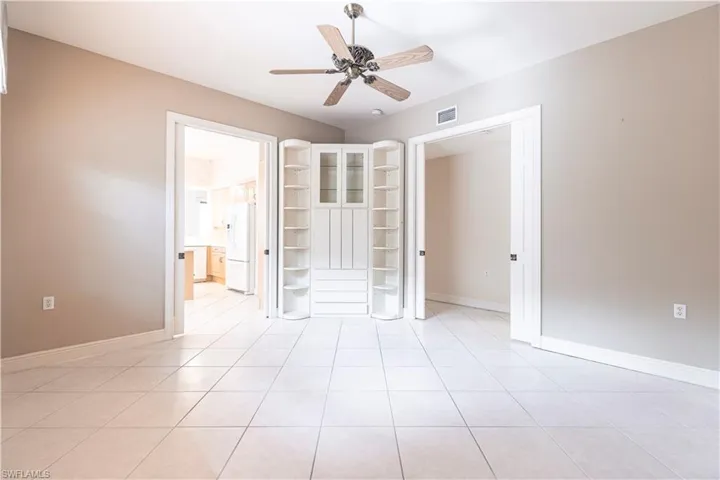 Unfurnished bedroom featuring white fridge with ice dispenser, light tile patterned floors, baseboards, ceiling fan, and connected bathroom