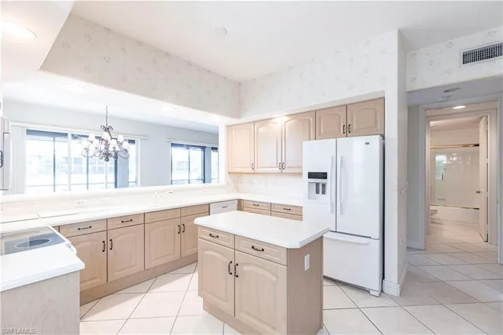 Kitchen featuring white appliances, light brown cabinets, a sink, a chandelier, and light tile patterned floors