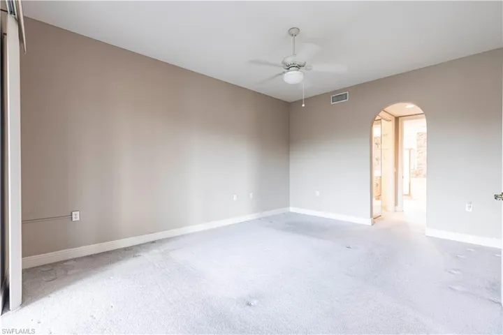 Spare room featuring arched walkways, a ceiling fan, light carpet, and baseboards