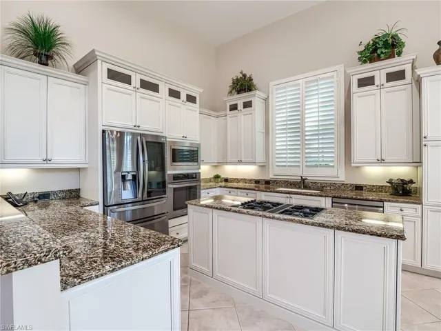 Kitchen with dark stone countertops, appliances with stainless steel finishes, white cabinetry, and light tile flooring