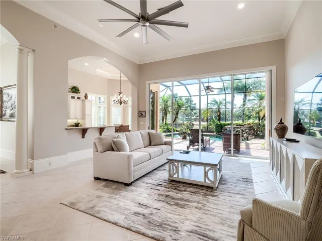 Tiled living room with ornamental molding, decorative columns, and ceiling fan with notable chandelier