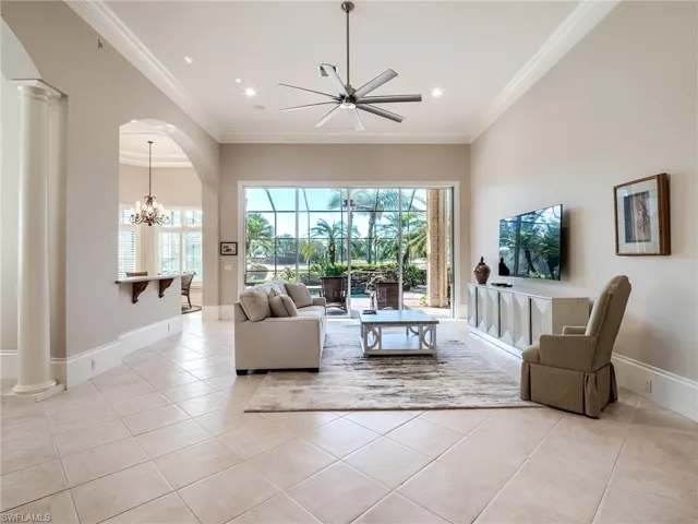 Living room with light tile flooring, decorative columns, and ceiling fan with notable chandelier