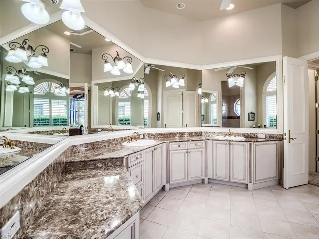 Bathroom featuring double sink vanity, a high ceiling, tile floors, and ceiling fan with notable chandelier