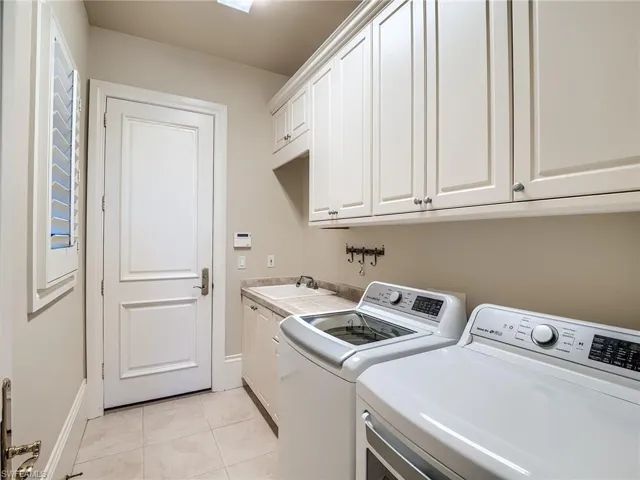 Laundry area with sink, independent washer and dryer, light tile floors, and cabinets