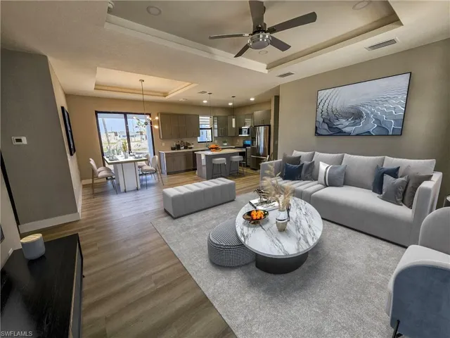 Living room with hardwood / wood-style flooring, ceiling fan with notable chandelier, and a raised ceiling
