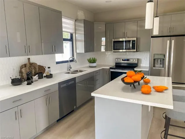 Kitchen with stainless steel appliances, gray cabinets, hanging light fixtures, and sink