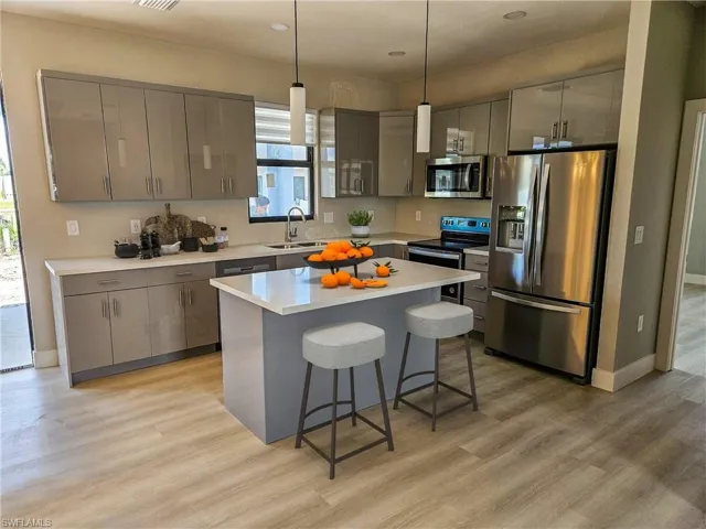 Kitchen featuring a center island, light wood-type flooring, decorative light fixtures, a kitchen bar, and stainless steel appliances
