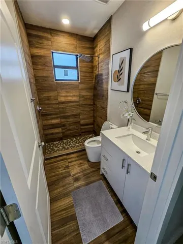Bathroom with hardwood / wood-style floors, vanity, toilet, and a tile shower