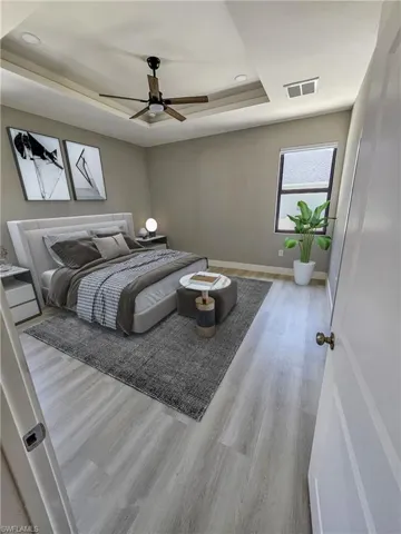 Bedroom featuring light hardwood / wood-style floors, ceiling fan, and a tray ceiling
