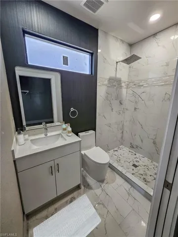 Bathroom featuring a tile shower, vanity, and toilet