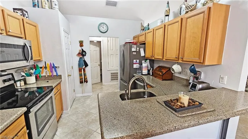 Kitchen with sink, light stone counters, light tile patterned floors, appliances with stainless steel finishes, and kitchen peninsula