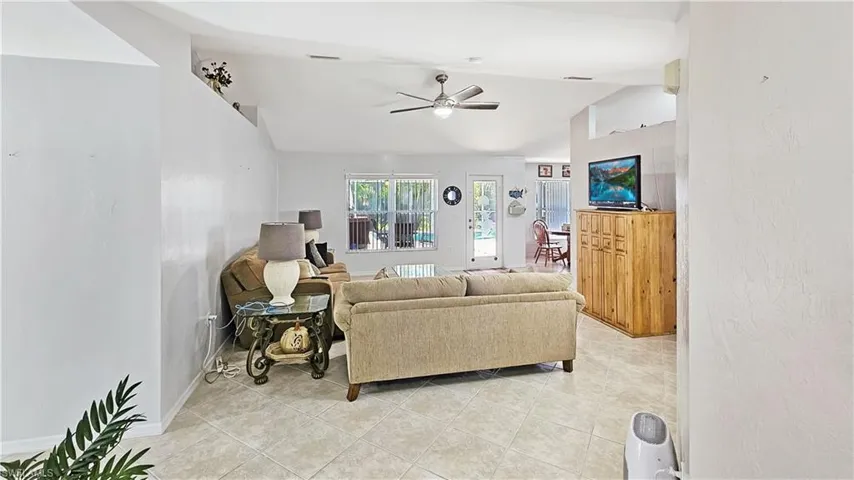 Living room with light tile patterned flooring, ceiling fan, and vaulted ceiling