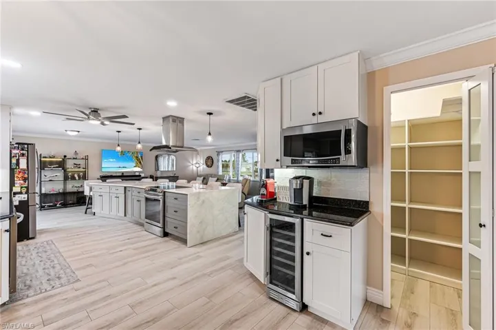 Kitchen with wine cooler, white cabinets, coffee and wine bar, large pantry, appliances with stainless steel finishes, island exhaust hood, and ornamental molding