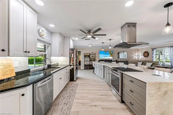 Kitchen with sink, island exhaust hood, dark granite countertops, and appliances with stainless steel finishes