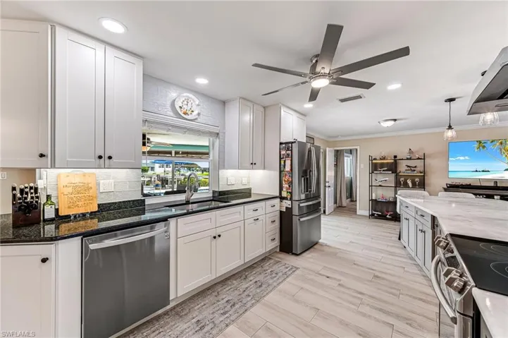 Kitchen featuring dark granite counters, tasteful backsplash, stainless steel appliances, white cabinets, and sink