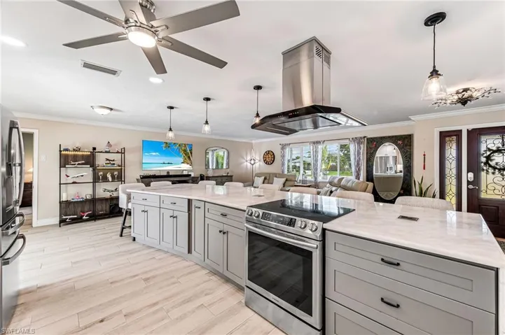 Kitchen with gray cabinetry, light marble counters, island exhaust hood, and electric stove