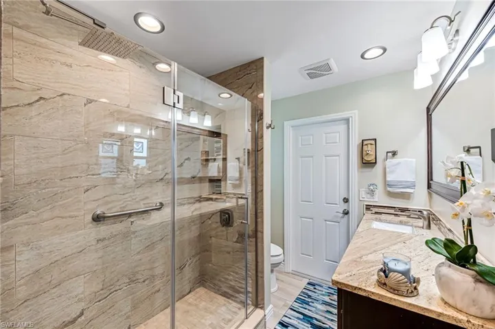 Bathroom with single vanity, a shower with glass shower door, and toilet