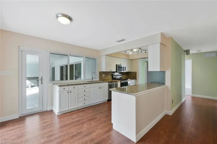Kitchen with dark wood-style flooring, stainless steel appliances, decorative backsplash, a peninsula, and white cabinets