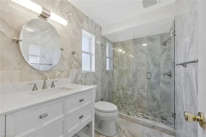 Bathroom featuring vanity, a marble finish shower, and tile walls