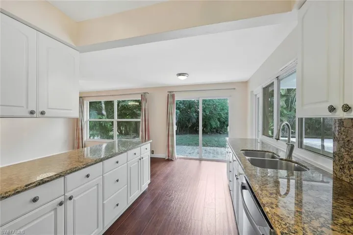 Kitchen with white cabinetry, light stone countertops, dark wood-style floors, and stainless steel dishwasher