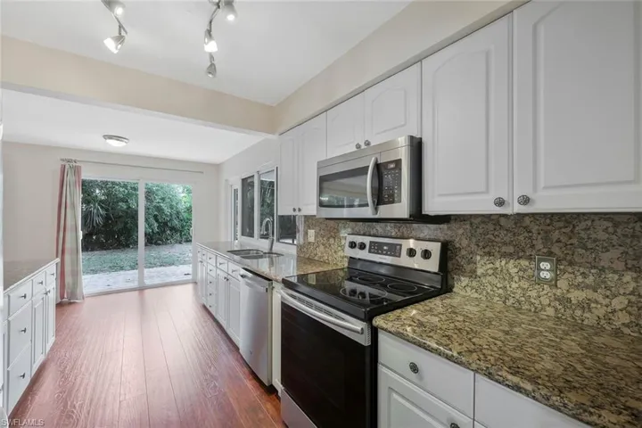 Kitchen with stainless steel appliances, white cabinetry, dark wood-style floors, and dark stone countertops