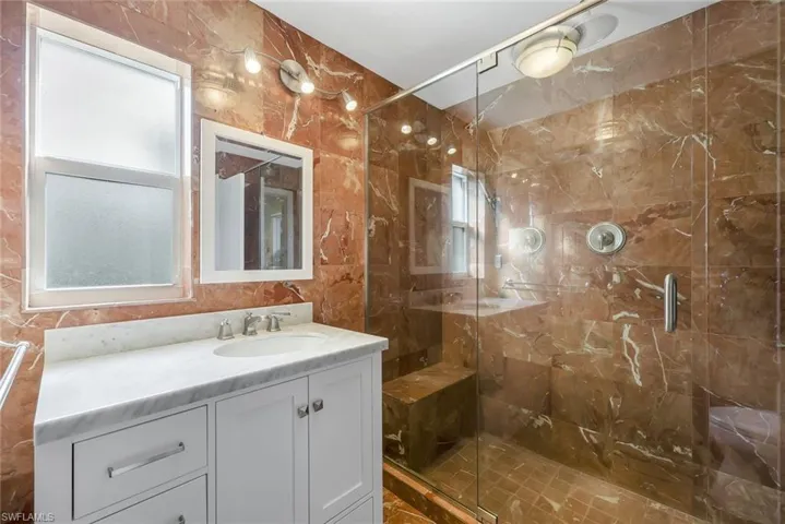 Bathroom with vanity, a marble finish shower, plenty of natural light, and tile walls