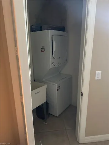 Laundry area with stacked washer and clothes dryer and light tile patterned floors