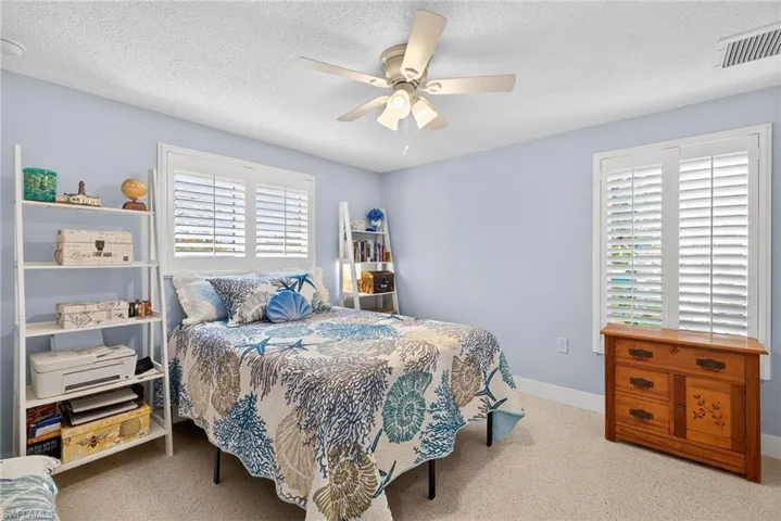 Bedroom with light carpet, multiple windows, ceiling fan, and a textured ceiling
