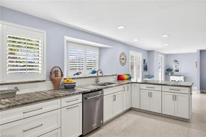 Kitchen with dark stone counters, stainless steel dishwasher, dark speckled floor, white cabinetry, and recessed lighting