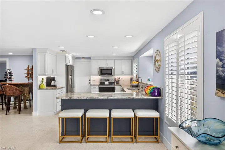 Kitchen with light stone counters, a peninsula, a kitchen breakfast bar, stainless steel appliances, and white cabinetry