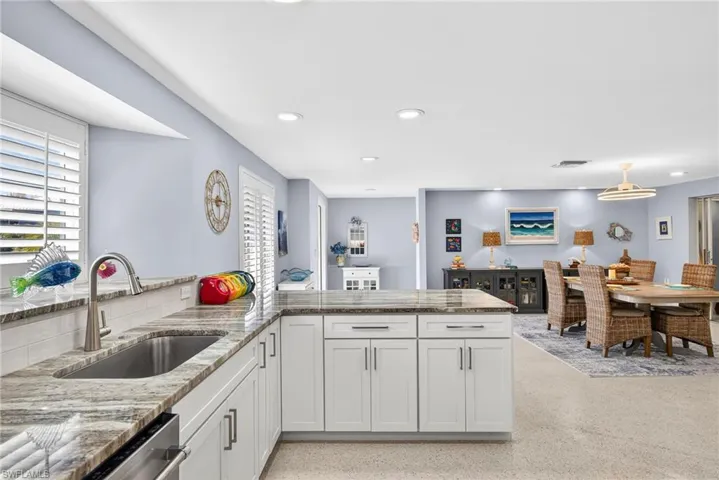 Kitchen featuring light stone countertops, a peninsula, dark speckled floor, white cabinetry, and plenty of natural light