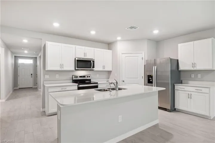 Kitchen featuring appliances with stainless steel finishes, light hardwood / wood-style flooring, white cabinets, sink, and an island with sink