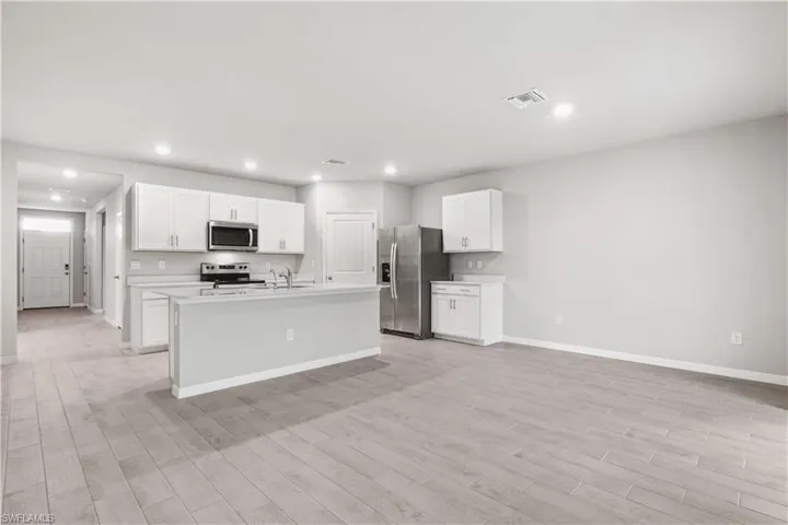 Kitchen featuring light hardwood / wood-style flooring, white cabinets, an island with sink, and stainless steel appliances