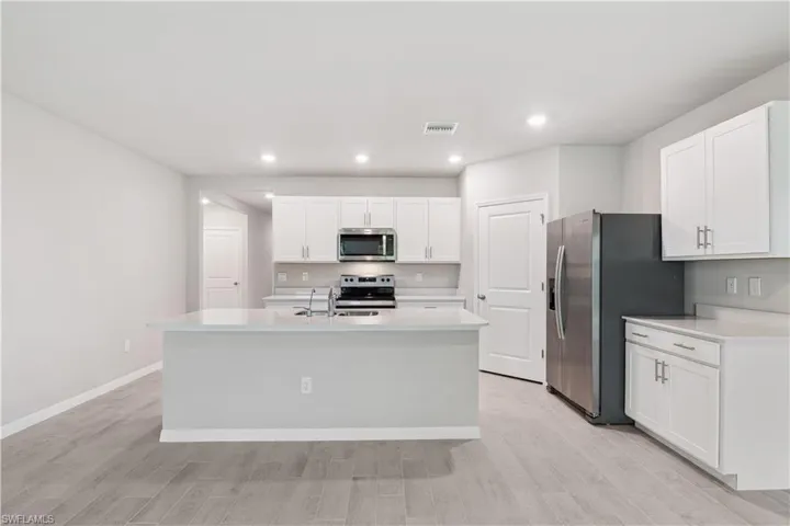 Kitchen with a kitchen island with sink, light wood-type flooring, stainless steel appliances, and white cabinets