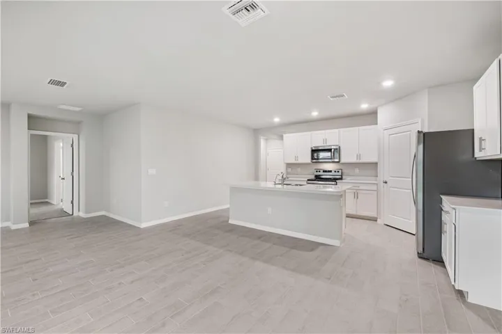 Kitchen with appliances with stainless steel finishes, sink, light wood-type flooring, an island with sink, and white cabinetry