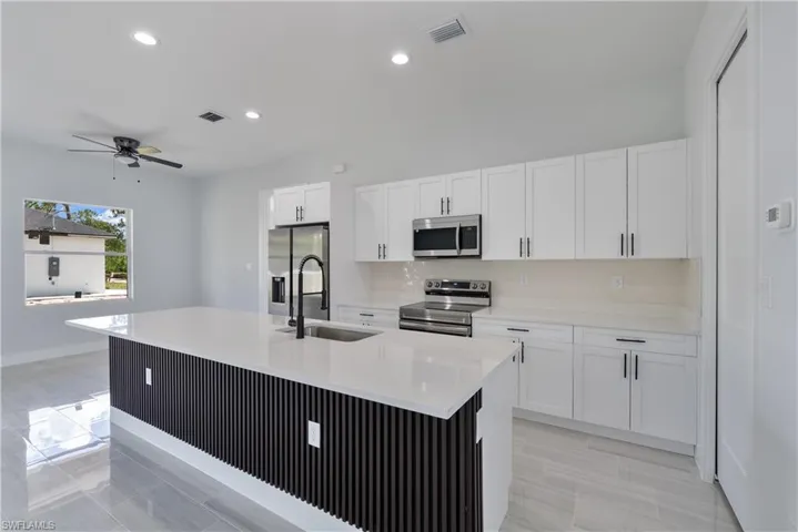 Kitchen featuring stainless steel appliances, white cabinets, ceiling fan, light countertops, and decorative backsplash