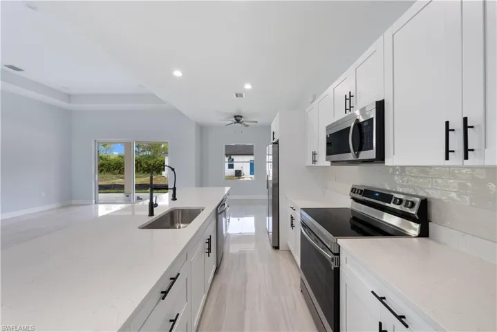 Kitchen featuring stainless steel appliances, recessed lighting, backsplash, light stone counters, and white cabinetry
