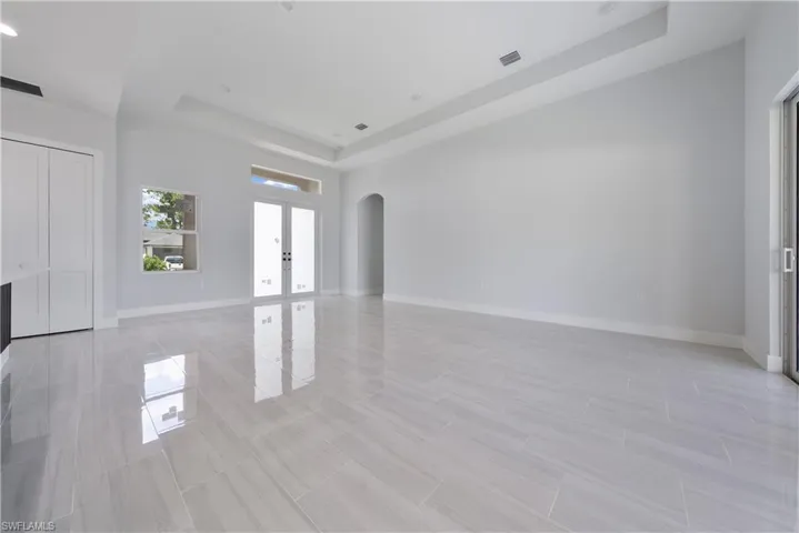 Empty room featuring a tray ceiling, arched walkways, and french doors