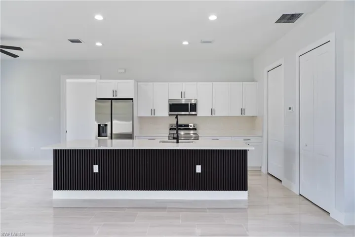 Kitchen featuring appliances with stainless steel finishes, white cabinetry, light countertops, a center island with sink, and recessed lighting