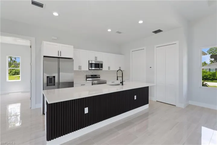 Kitchen with white cabinets, stainless steel appliances, backsplash, light countertops, and an island with sink