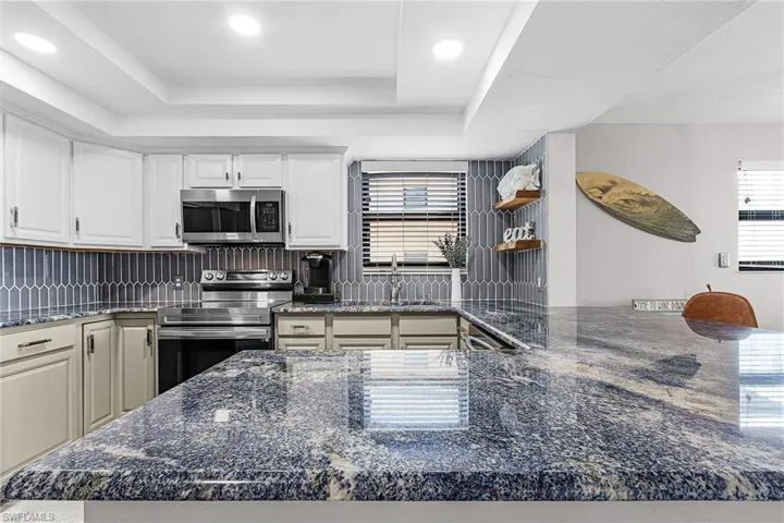 Kitchen with dark stone counters, stainless steel appliances, white cabinetry, recessed lighting, and a raised ceiling