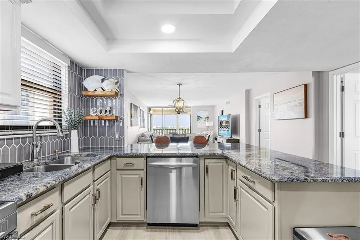 Kitchen featuring dishwasher, dark stone countertops, a raised ceiling, open floor plan, and open shelves
