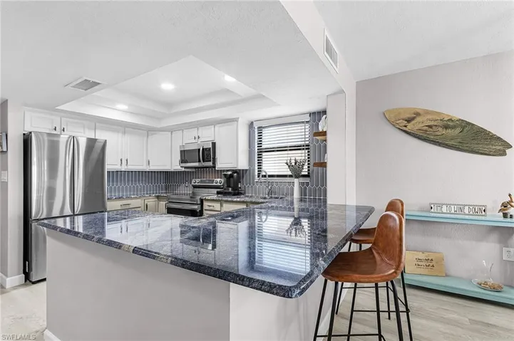 Kitchen featuring white cabinets, a breakfast bar area, light wood-type flooring, stainless steel appliances, and a raised ceiling