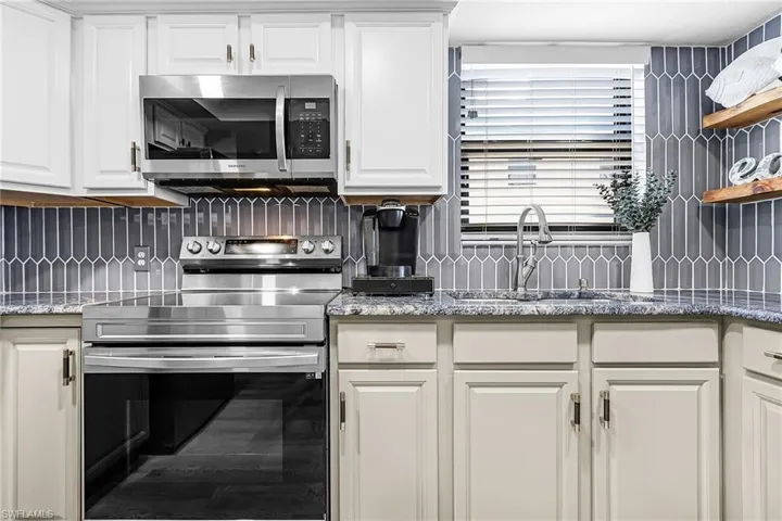 Kitchen featuring stainless steel appliances, dark stone countertops, white cabinetry, open shelves, and tasteful backsplash