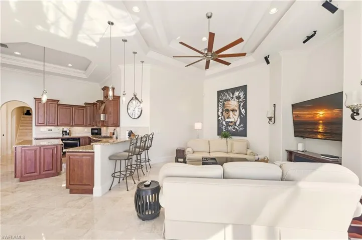 Living area featuring a raised ceiling, arched walkways, crown molding, a ceiling fan, and recessed lighting