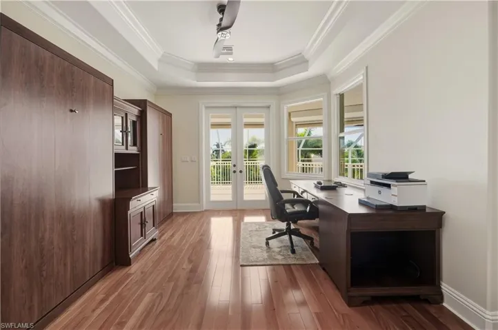Office space with light wood-style flooring, french doors, a tray ceiling, and ornamental molding